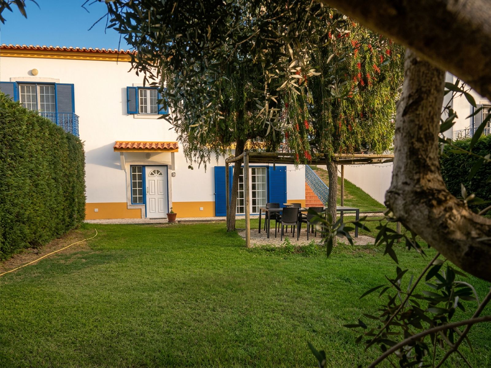 M&M House: casa branca com barra amarela e portadas azuis, vista do jardim privado